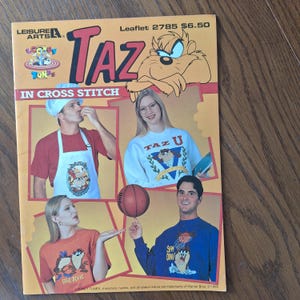 May include: A cross stitch pattern booklet featuring Taz, the Tasmanian Devil, from Looney Tunes. The cover shows Taz in a variety of poses, including a basketball player, a chef, and a college student. The booklet is titled "Taz in Cross Stitch" and includes the text "Looney Tunes, characters, names, and all related indicia are trademarks of Warner Bros. © 1995."