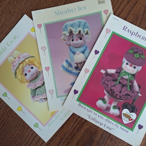 May include: Three crochet pattern booklets titled Sherbet Ice, Bubble Gum, and Raspberry, each featuring a doll illustration with colorful yarn outfits, hats, and accessories, with the text Brought to you directly from Lollipop Lane.