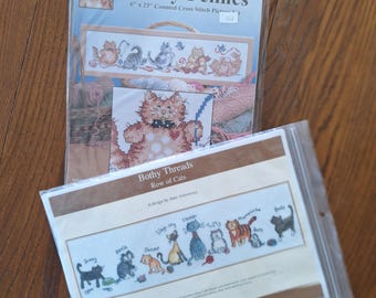 May include: Two cross stitch patterns featuring cats. The first pattern is titled "Frisky Felines" and shows a row of five cats. The second pattern is titled "Bothy Threads Row of Cats" and shows a row of nine cats.