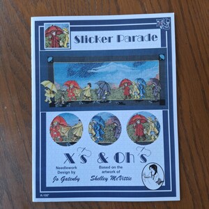 Op de afbeelding: Een borduurpatroon getiteld "Slicker Parade" met de tekst "X's & Oh's". Het ontwerp toont illustraties van mensen die in de regen lopen onder paraplu's. Het kunstwerk is van Shelley McVittie en ontworpen door Jo Gatenby.