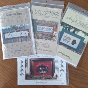 Peut inclure: Quatre motifs de point de croix différents pour des travaux manuels de Noël. Les motifs sont intitulés "Reindeer Ballad", "Merry Christmas to You", "Tis the Season" et "Merry Christmas is Here".