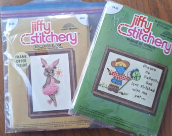 Peut inclure: Deux kits de point de croix Jiffy Stitchery. L'un représente un lapin ballerine, l'autre un cow-boy avec le texte "Please Be Patient, God isn't finished with me yet...". Les deux kits sont dans un emballage plastique avec l'étiquette de prix visible.