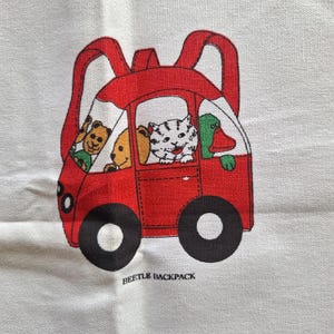 May include: A red backpack with a cartoon car design. The car has black wheels and carries a cat, a duck, and two teddy bears. The text "BEETLE BACKPACK" is printed below the car.