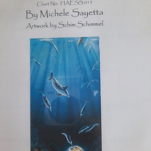Puede incluir: Un patrón de punto de cruz que representa una escena de océano azul con delfines nadando alrededor de un globo terráqueo. El título del patrón es "Sunken Treasure" y el número de la carta es HAESS 015. La artista es Michele Sayetta y la obra de arte es de Schim Schimmel.