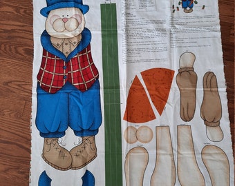 May include: A white fabric panel with instructions for making a bunny door panel. The panel features a cartoon bunny wearing a blue hat, red and black plaid vest, and blue pants. The panel also includes pattern pieces for the bunny's head, ears, arms, and legs.