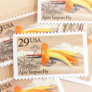 Può includere: Diversi francobolli 29 USA con un disegno Apte Tarpon Fly. I francobolli hanno uno sfondo beige con un'illustrazione di mosca da pesca arancione e gialla. Il testo "Apte Tarpon Fly" è stampato sul francobollo.
