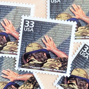 Pode incluir: Um conjunto de quatro selos postais dos Estados Unidos de 33 centavos com um soldado em camuflagem tocando um muro do Memorial dos Veteranos do Vietnã. O muro está inscrito com os nomes dos soldados. Os selos são brancos com detalhes vermelhos, azuis e pretos.