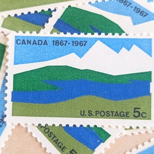 Op de afbeelding: Een verzameling vintage postzegels met een landschapsontwerp. De postzegels hebben een blauw, groen en wit kleurenschema, met de tekst "CANADA 1867-1967" en "U.S. POSTAGE 5c".