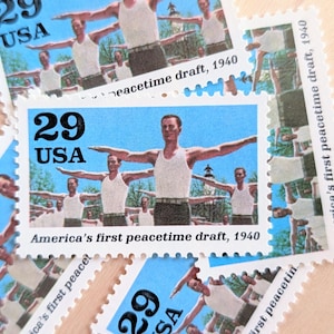 Könnte beinhalten: Eine Sammlung von 29-Cent-USA-Briefmarken. Jede Briefmarke zeigt einen Mann in einem weißen Tanktop mit ausgestreckten Armen vor blauem Hintergrund. Text: "America's first peacetime draft, 1940."