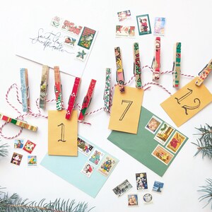 May include: A Christmas advent calendar made with clothespins decorated with colorful patterned paper and numbered tags. The clothespins are strung with twine and hang from a white surface. The numbers on the tags are 1, 7, and 12.