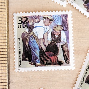 May include: A vintage 32 cent US postage stamp with the text "Prohibition Enforced" and the year 1998. The stamp features a colorful illustration of two men pouring wine from a barrel into a sewer drain.