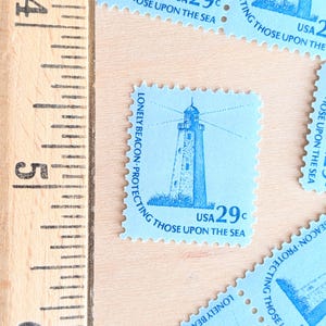 May include: Light blue postage stamps with a lighthouse design and the text "LONELY BEACON PROTECTING THOSE UPON THE SEA" and "USA 29c". A wooden ruler is in the frame.