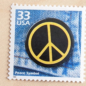 May include: A 33 cent USA postage stamp featuring a black peace symbol with a yellow outline on a blue denim background. The text "Peace Symbol" and "1999" are printed below the symbol.