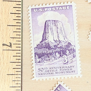 May include: A collection of vintage U.S. postage stamps. The primary stamp features a purple illustration of Devils Tower National Monument, with the text "U.S. POSTAGE" and "50th Anniversary Devils Tower National Monument". The stamp is valued at 3 cents.