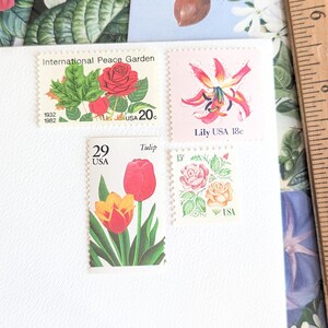 Puede incluir: Cuatro sellos postales vintage con diseños florales, incluyendo un sello del International Peace Garden, uno de lirio, uno de tulipán y uno de rosa, dispuestos sobre una superficie blanca junto a una regla de madera con medidas en centímetros.