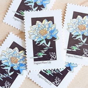 May include: Four vintage postage stamps featuring a blue and yellow water lily with green leaves on a black background. The stamps are all marked "USA 29" and "Fragrant Water Lily".
