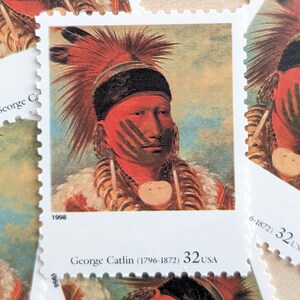 May include: A vintage United States postage stamp featuring a portrait of a Native American man with red and black face paint. The stamp is from 1998 and features the text "George Catlin (1796-1872) 32 USA".