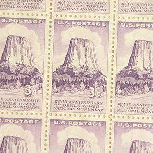 May include: Nine purple and white postage stamps featuring a picture of Devils Tower National Monument. Each stamp reads "50th Anniversary Devils Tower National Monument" and "U.S. Postage" with a 3 cent denomination.