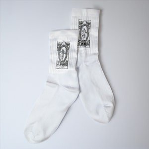 May include: A pair of white socks with black and white tarot card designs. The socks feature the "Le-Homme" card.