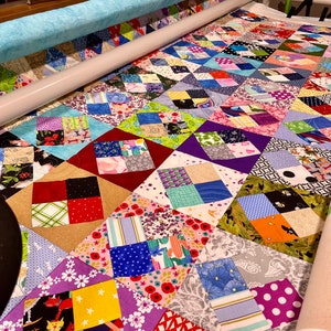 Pode incluir: Um cobertor com um design de patchwork que apresenta uma variedade de tecidos coloridos. O cobertor est&aacute; sendo acolchoado em uma m&aacute;quina de acolchoar de bra&ccedil;o longo.