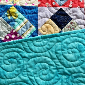 Pode incluir: Uma colcha azul turquesa com um padr&atilde;o de espiral. A colcha &eacute; feita de v&aacute;rios quadrados de tecido com padr&otilde;es e cores diferentes, incluindo vermelho, amarelo, azul e branco.
