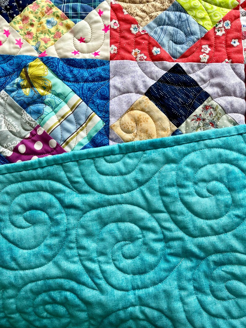 Pode incluir: Uma colcha azul turquesa com um padr&atilde;o de espiral. A colcha &eacute; feita de v&aacute;rios quadrados de tecido com padr&otilde;es e cores diferentes, incluindo vermelho, amarelo, azul e branco.