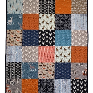 May include: A patchwork quilt featuring a range of woodland animal and nature-inspired designs in shades of blue, grey, orange, and red. The quilt is composed of 25 squares, each with a unique pattern.