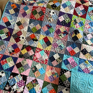 Pode incluir: Uma colcha de retalhos colorida com uma variedade de tecidos e padr&otilde;es. A colcha &eacute; feita de quadrados e diamantes, e &eacute; acolchoada com um padr&atilde;o de redemoinho. A colcha &eacute; de cor azul claro e est&aacute; dobrada ao meio.