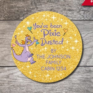 May include: A circular gold glitter sticker featuring a purple dragon illustration, white star accents, and the text: You've been Pixie Dusted BY THE JOHNSON FAMILY CABIN 1234. The design includes small colorful balloon icons.