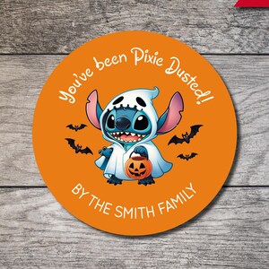 May include: A circular orange sticker featuring a blue alien character wearing a white ghost costume and holding a small orange jack-o'-lantern bucket. The text reads You've been Pixie Dusted! and BY THE SMITH FAMILY, surrounded by black bat silhouettes.