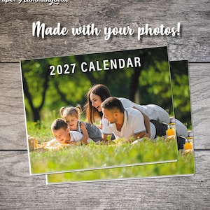 May include: A custom 2027 calendar featuring a photograph of a family lying in the grass. The text "The Paper Hummingbird" appears at the top left, and the phrase "Made with your photos!" is centered above the calendar cover image.