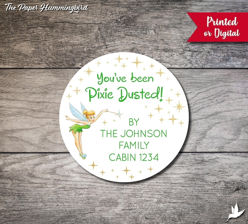 May include: A white round sticker featuring a green Tinkerbell illustration and gold glitter stars. The text reads "You've been Pixie Dusted!" with the words "BY THE JOHNSON FAMILY CABIN 1234" below.