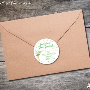 May include: A white round sticker with a green fairy illustration and gold glitter. The sticker says "You've been Pixie Dusted!" and "By The Johnson Family Cabin 1234".