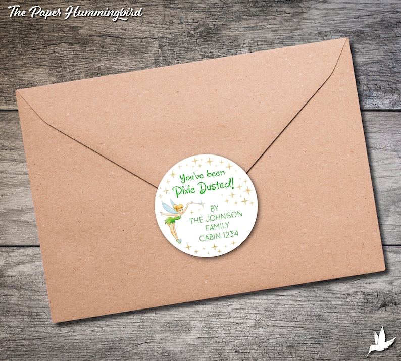 May include: A white round sticker with a green fairy illustration and gold glitter. The sticker says "You've been Pixie Dusted!" and "By The Johnson Family Cabin 1234".