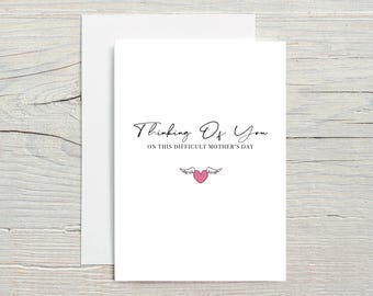 May include: A white card with black text that reads "Thinking of you on this difficult Mother's Day". A small pink heart with wings is below the text.