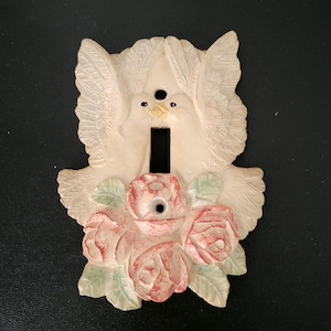 May include: Off-white light switch cover featuring two doves with outstretched wings and a cluster of pink roses with green leaves. The switch plate has a rectangular opening for the switch and two screw holes.