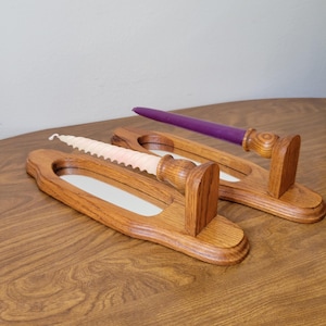 May include: Two wooden candle holders with a light brown finish. One holder has a pink, spiral-shaped candle, and the other has a purple candle. The holders have a rectangular base with a mirrored insert.