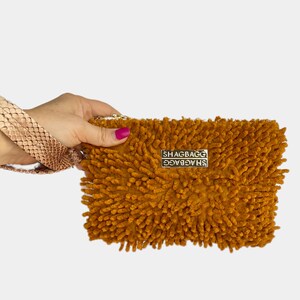 Pode incluir: Uma bolsa de mão de pelo amarelo mostarda com um fecho de correr de metal dourado e o texto "SHAGBAG" impresso na frente.