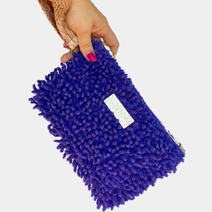 May include: A purple shaggy fabric pouch with a gold zipper and a silver tag that reads "SHAGBAG" in all caps.