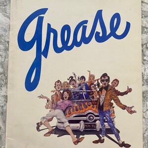 May include: A vintage-style program cover for the musical "Grease" featuring a cartoon illustration of a group of people in a hot rod car. The car is red with flames and the title "Grease" is written in blue cursive.