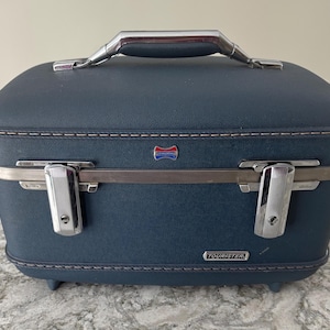 May include: A vintage navy blue Tourister suitcase with a silver handle and hardware. The suitcase has a rounded top, a textured surface, and a small emblem. The Tourister logo is visible on the front.
