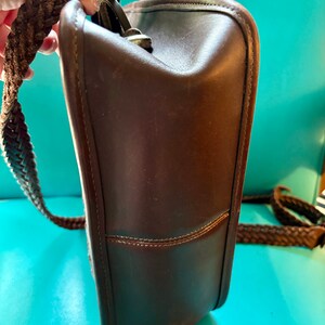 Puede incluir: Un bolso de hombro de cuero marr&oacute;n con una correa trenzada. El bolso tiene un cierre de solapa y un compartimento &uacute;nico.