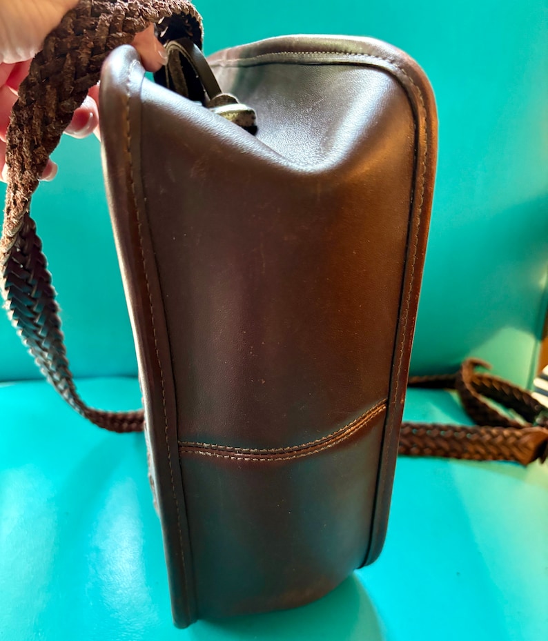 Puede incluir: Un bolso de hombro de cuero marr&oacute;n con una correa trenzada. El bolso tiene un cierre de solapa y un compartimento &uacute;nico.