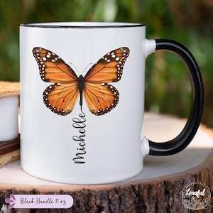 Peut inclure: Une tasse en c&eacute;ramique blanche avec une anse noire. La tasse pr&eacute;sente un papillon color&eacute; aux ailes orange, noires et blanches. Le mot "Michelle" est &eacute;crit verticalement sous le papillon.