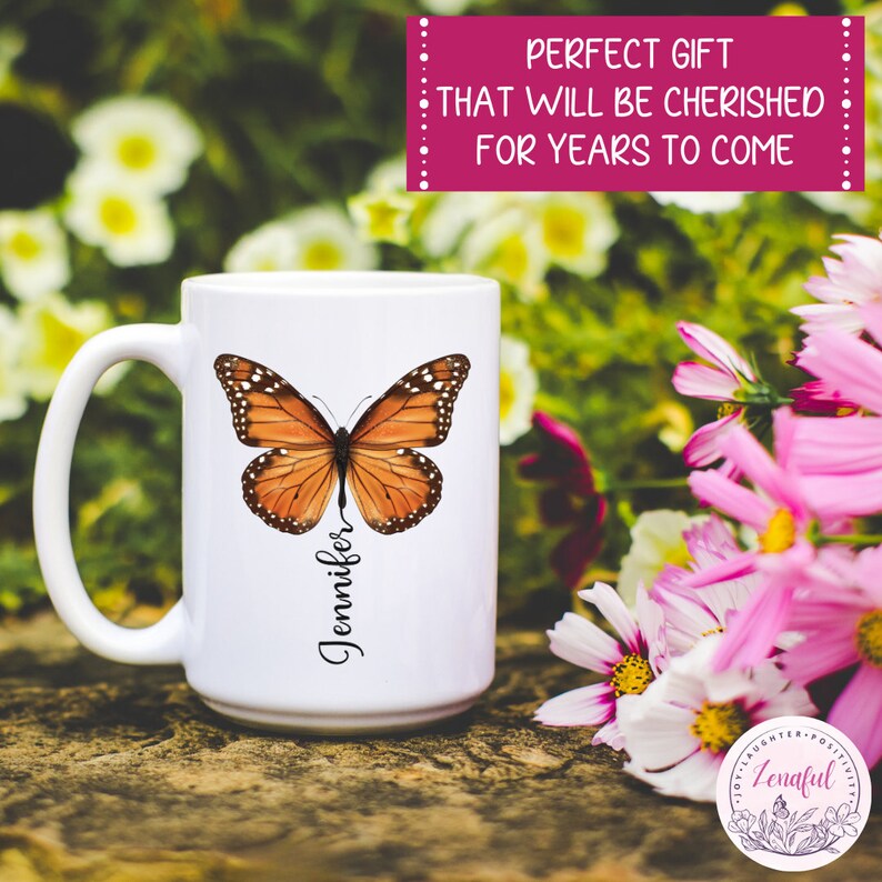 Peut inclure: Une tasse en c&eacute;ramique blanche avec un motif de papillon brun et le nom "Jennifer" &eacute;crit verticalement sur le c&ocirc;t&eacute;. La tasse est pos&eacute;e sur une surface en bois avec des fleurs roses et blanches en arri&egrave;re-plan.