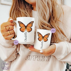 Peut inclure: Deux tasses en c&eacute;ramique blanche avec un motif de papillon et le nom "Charlotte" imprim&eacute; dessus. La tasse de gauche est de 15 oz et la tasse de droite est de 11 oz.