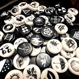 May include: A collection of black and white round tokens with various symbols and numbers. The tokens are made of plastic or metal and have a glossy finish.