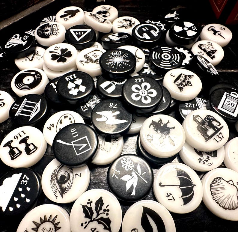 May include: A collection of black and white round tokens with various symbols and numbers. The tokens are made of plastic or metal and have a glossy finish.