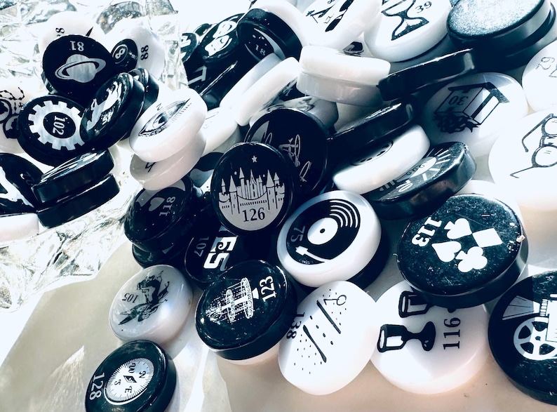 May include: A collection of black and white round tokens with various symbols and numbers. The tokens are made of a smooth, glossy material and have a raised design. Some of the numbers on the tokens include 39, 30, 113, 116, 75, 88, 126, 138, 123, 107, 81, 118, 102, 105, 128.
