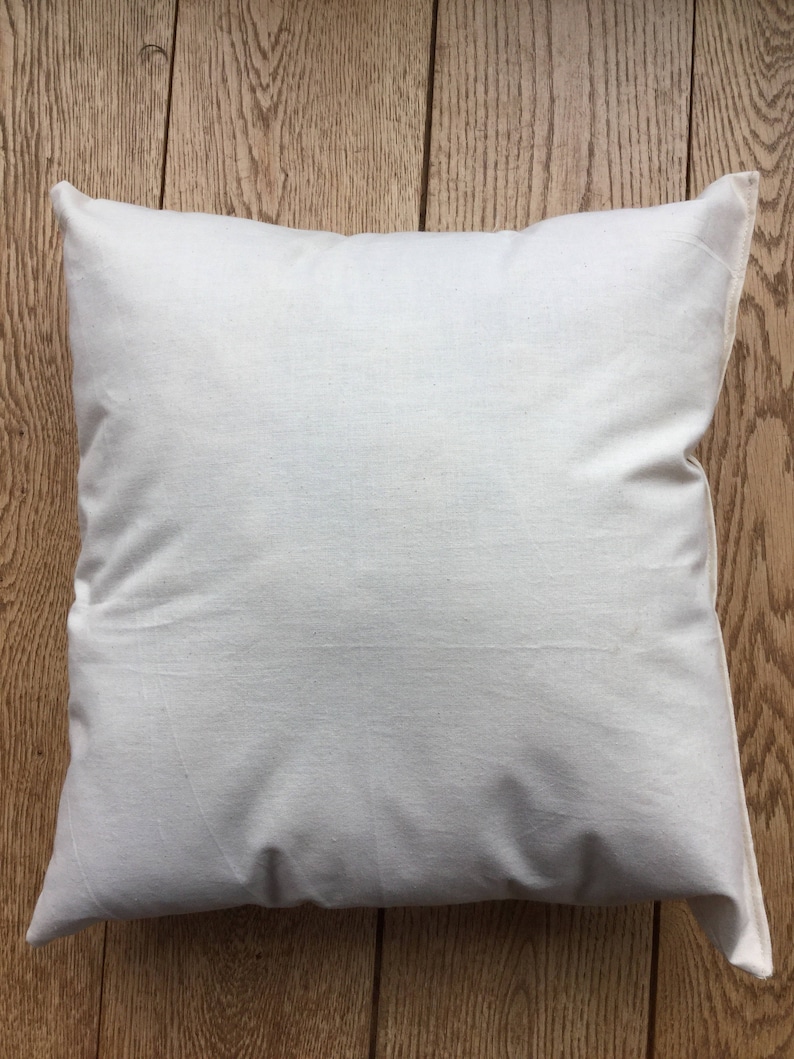 May include: A square throw pillow cover made of plain, off-white, unbleached cotton fabric. The pillow cover features a simple, seamless design with a visible texture characteristic of natural woven cotton fibers, presented in a clean, neutral tone.